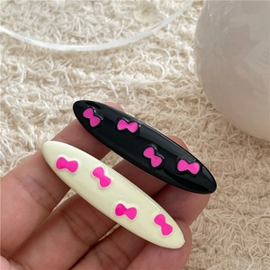 Sweet pink bow pattern on black and cream oval hair clips held in hand