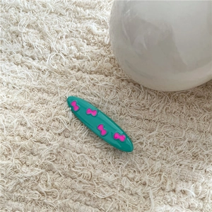 Detail of green oval hair clip with pink bow patterns on a soft white plush background