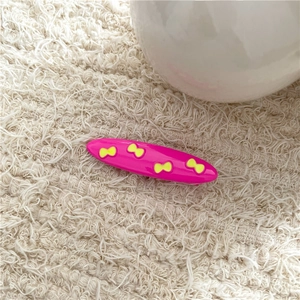 Detail of a bright pink alloy hair clip with yellow butterfly patterns on soft fabric
