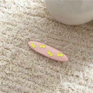 Close-up of pink alloy hair clip with yellow butterfly patterns on soft fabric background