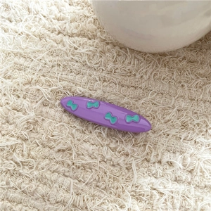 Detail of purple hair clip with green 3D bow patterns on white knit fabric background