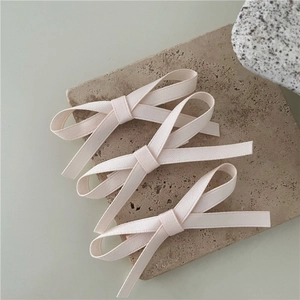 Detailed view of three cream fabric bow hair clips arranged on a textured stone plate