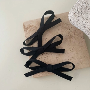 Detailed macro view of three black ribbon bow hair clips on minimalist stone surface