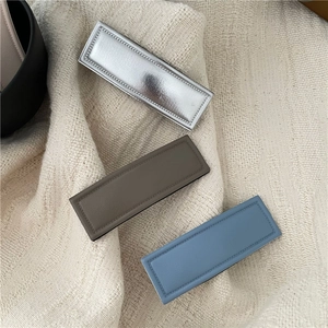 Three textured PU leather and metallic rectangle hair clips on beige knit fabric