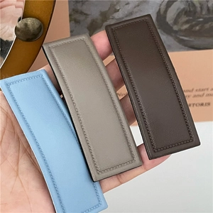 Detail view of rectangular PU leather hair clips in blue, grey, and brown with stitching