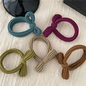 Detail of five assorted morandi color ribbed knit bow hair ties on a linen fabric surface