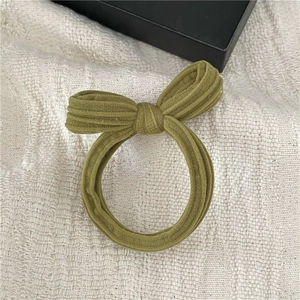 Detail of dark green bow scrunchie with striped velvet texture on creamy fabric