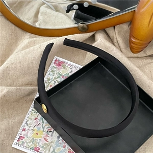 Detailed view of black satin headband with decorative golden circular metal piece