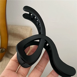 Matte black geometric hair claw clip with twisted minimalist design held in hand