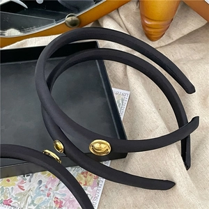 Close-up of black satin headband featuring a gold metallic smiley face charm detail