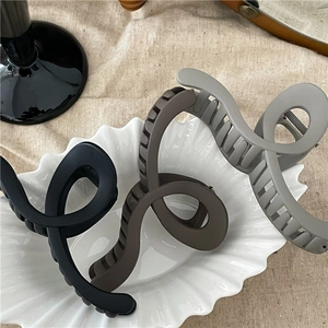 Detail of matte geometric S-shaped hair claws in Morandi tones on a white ceramic tray
