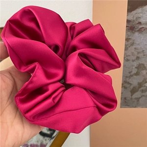 Detail eines großen magentafarbenen Satin-Haargummis mit glänzender Textur und Falten-Design