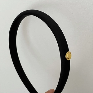 Detail view of black satin headband with minimalist golden round metal decorative piece