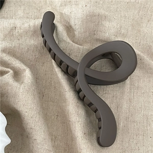 Detail view of large dark coffee matte claw clip with geometric twist design on beige linen