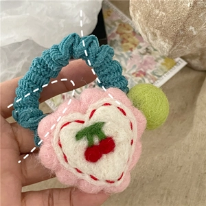 Detailed close-up of handmade knit hair tie with pink flower base and embroidered red cherries