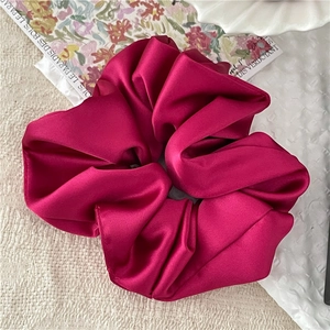 Makro-Detail von glänzendem magentafarbenem Satin-Scrunchie mit weicher Seidentextur