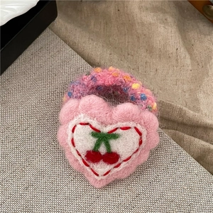 Detail eines rosa gestrickten Herz-Haargummis mit Kirschstickerei und Flausch
