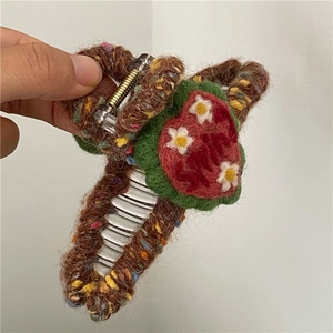 Detail view of the brown knitted hair claw clip with a red heart and white flower embroidery