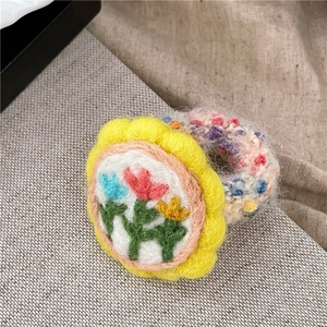 Detailansicht von gelbem Haargummi aus Wollfilz mit bunten gestickten Blumenmustern