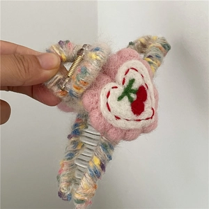 Detailed close-up of wool felt hair claw with heart pattern and pink plush flower decoration