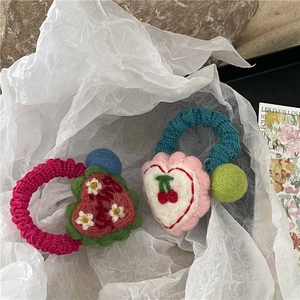 Detail of handmade crochet hair ties with colorful wool balls and heart-shaped floral patterns