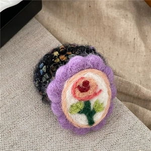 Detailaufnahme des handgefertigten lila Wollfilz Blumen-Haargummis mit Rosenstickerei