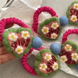 Close-up of wool felt heart hair tie with colorful pom-poms and cute floral details