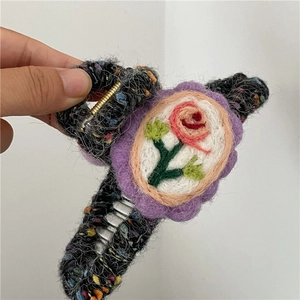 Close-up of large hair claw clip with wool felt floral embroidery and tweed fabric finish