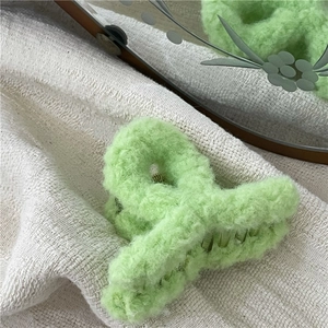 Detail shot of light green plush hair claw clip on white knitted fabric background
