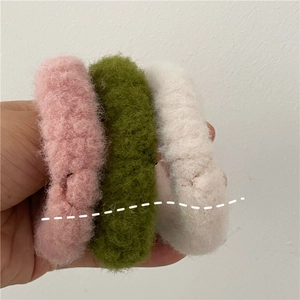 Close-up of soft plush hair scrunchies in cream pink, olive green, and off-white colors