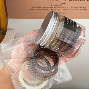 Jelly-textured spiral hair ties set in neutral tones of beige and brown in a plastic jar