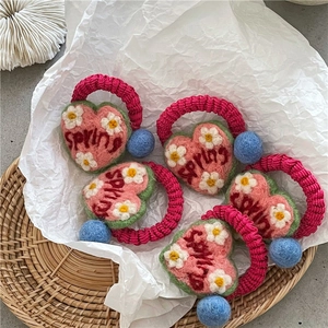 Detail of five handmade crochet heart hair ties with Spring embroidery and plush pom-poms