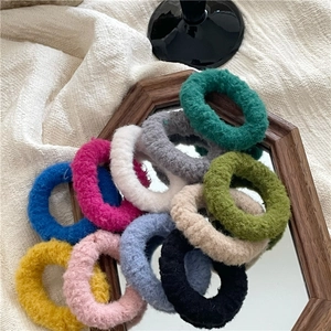 Pile of colorful plush hair scrunchies in cream tones on a wooden mirror tray