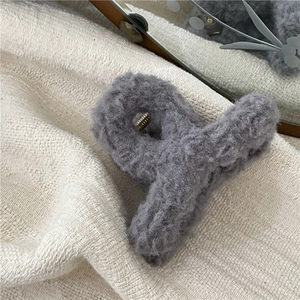 Close-up of fluffy grey plush hair claw clip with golden metal spring on white knit fabric