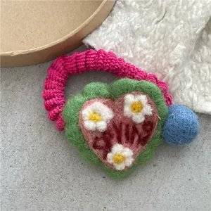 Detail of wool felt heart hair tie featuring knitted daisies and colorful pom poms