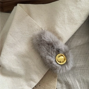 Detailed view of gray faux fur hair clip with a round golden metal accent