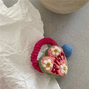 Detail of pink and green wool felt heart hair tie with baby embroidery and fuzzy ball