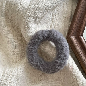 Close-up of soft grey plush scrunchie made of fluffy fabric on a striped textile background
