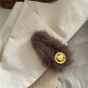 Detailed close-up of brown plush hair clip with a gold round metal emblem
