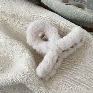 Close-up of plush cream-colored hair claw clip with golden metal spring and soft faux fur texture