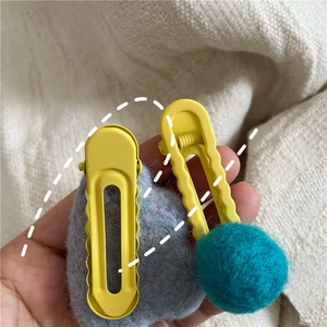 Detail view of yellow wave metal hair clip and turquoise pom-pom BB clip on fabric