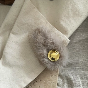 Detail view of khaki faux mink fur hair clip with a round golden metal emblem