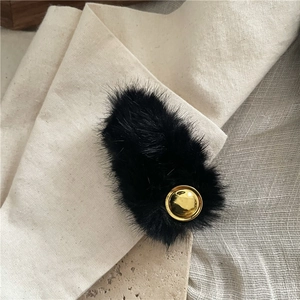 Close-up of black faux fur hair clip with golden round metallic detail on linen