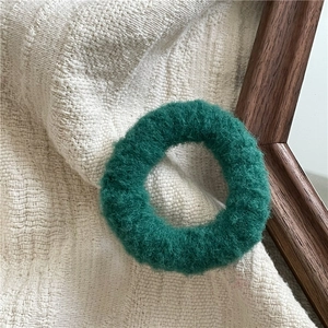 Macro shot of plush dark green hair scrunchie on knitted fabric with warm home decor