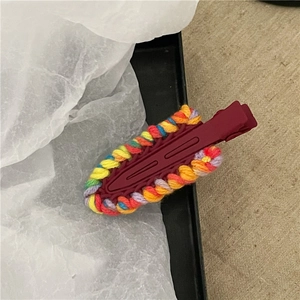 Dettaglio di un fermaglio per capelli rosso avvolto in filati colorati su carta velina