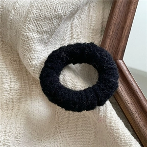 Close-up of a soft black plush hair tie placed on a textured cream waffle fabric background
