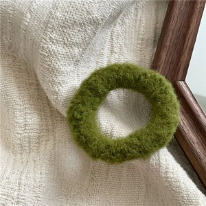 Close-up of a fluffy grass green plush hair scrunchie on cream textured fabric