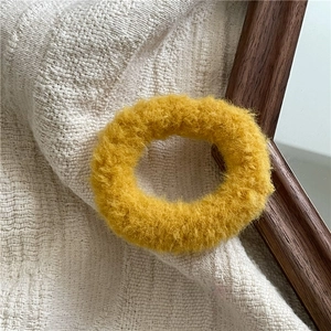 Close-up of a soft yellow plush hair tie on textured fabric with a wooden frame