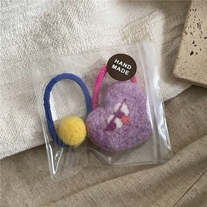 Detailed shot of handmade wool felt hair ties with heart and pompom in branded packaging
