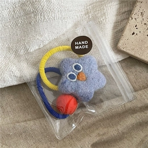 Detail of blue knitted star hair tie with big eyes and red pompom in handmade packaging